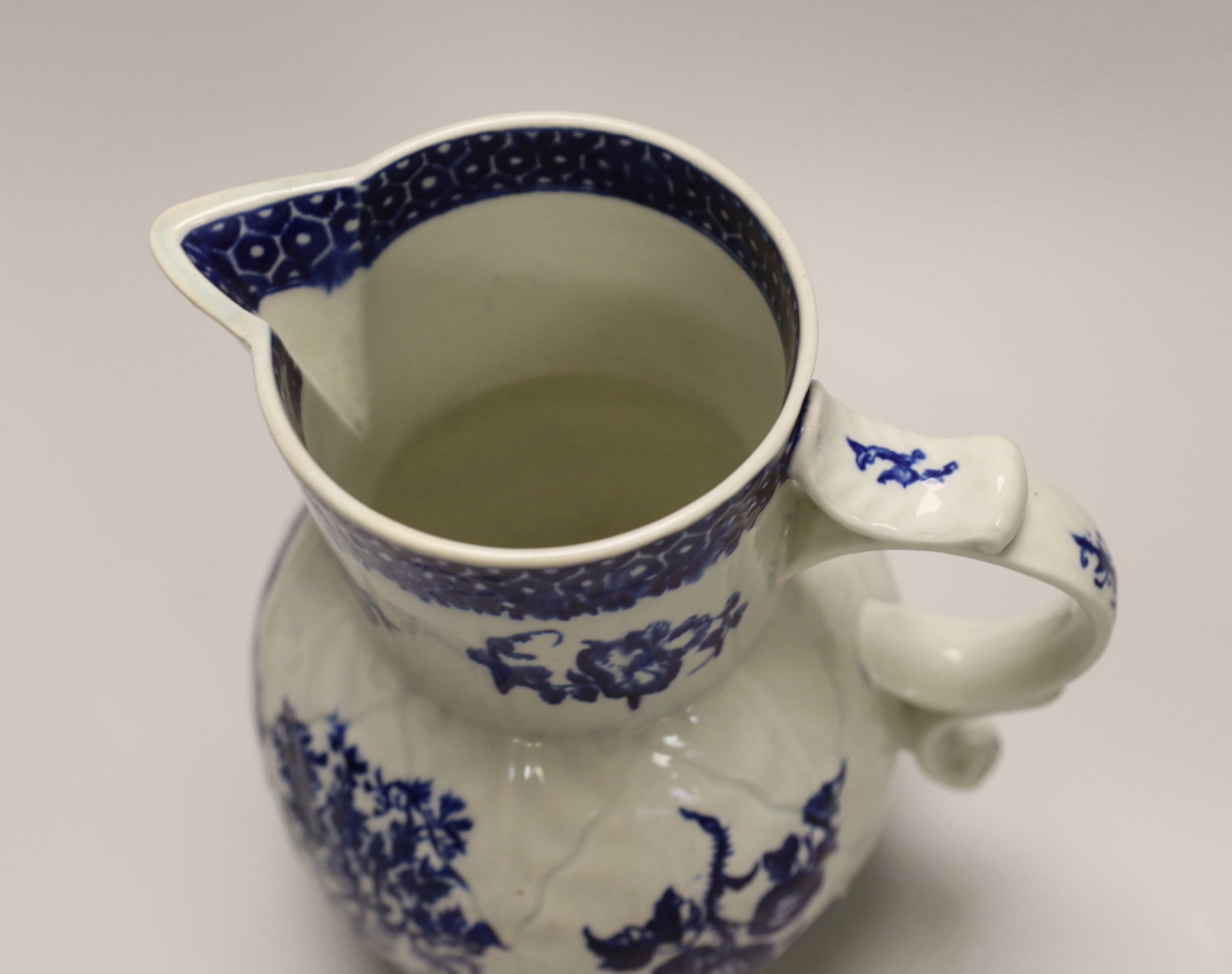 An 18th century Worcester fine mask jug decorated with the Parrot Pecking Fruit pattern, disguised numeral mark, 21cms high